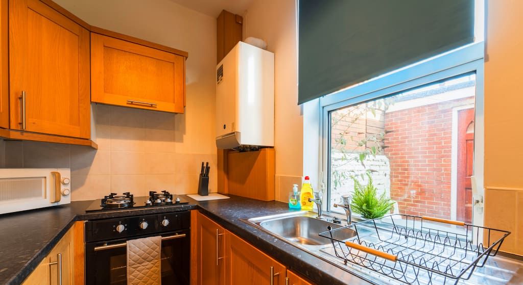 A kitchen with wooden cabinets, a stove, a microwave, and a window with a view of a brick building.