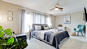 A modern bedroom with a large bed, a ceiling fan, a side table, and a chair. - Family friendly activities for all ages! Pool, Golf, Corn-Hole, Fishing & more! (Bradenton)