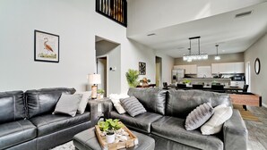 A modern living room with leather sofas, a coffee table with decorative items, and a dining area with a kitchen in the background. - Family friendly activities for all ages! Pool, Golf, Corn-Hole, Fishing & more! (Bradenton)