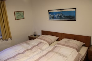 Una cama doble con cabecera de madera, una mesita de noche con lámpara, un mapa enmarcado y una imagen enmarcada de un paisaje montañoso.