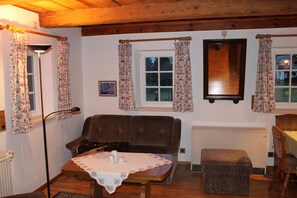 Una habitación acogedora con un sofá marrón, una mesita con mantel de encaje, una silla de madera y un radiador.