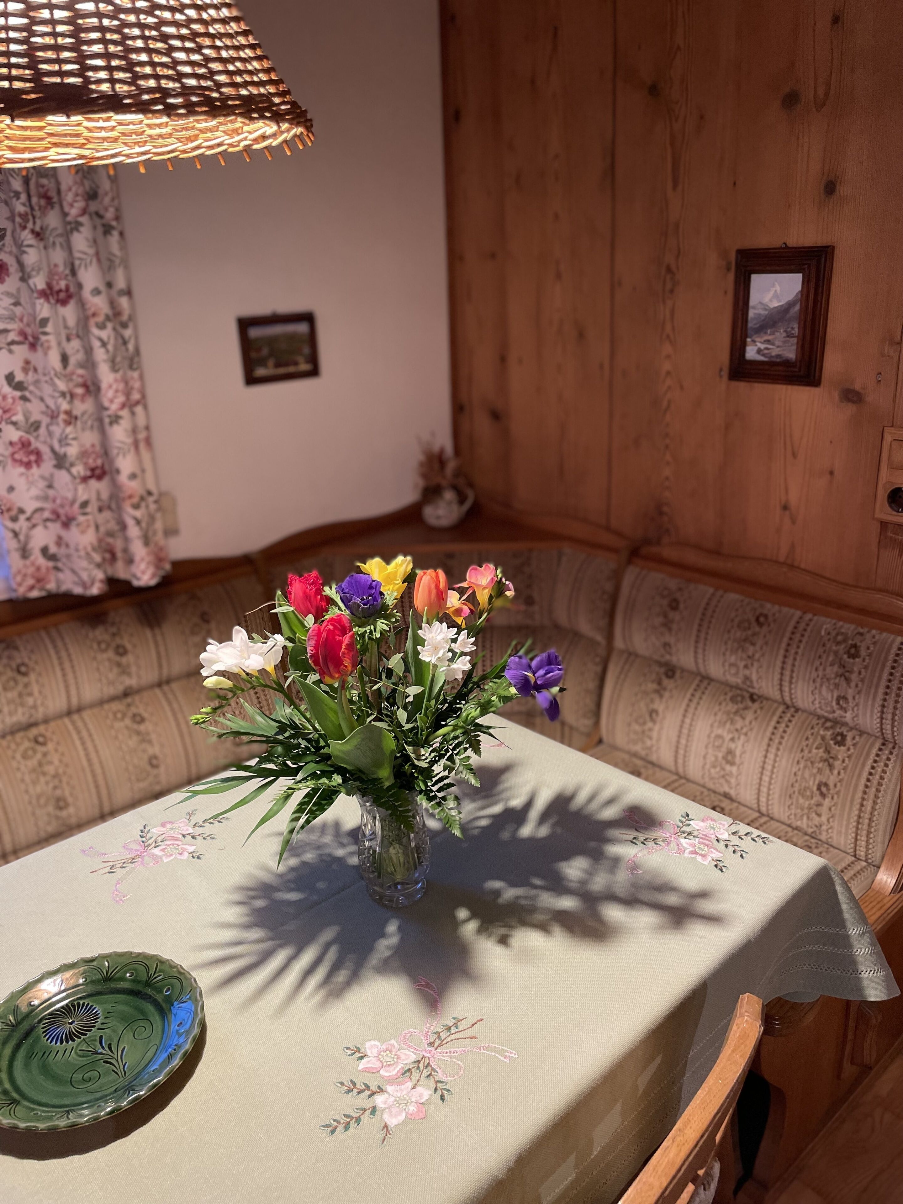 A corner of a room with a wooden wall, a floral-patterned sofa, and a table with a floral tablecloth.