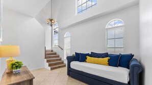 Ein geräumiger Wohnbereich mit Treppe, einem Sofa mit blau-gelben Kissen und einem Holztisch mit Lampe und Dekoration.