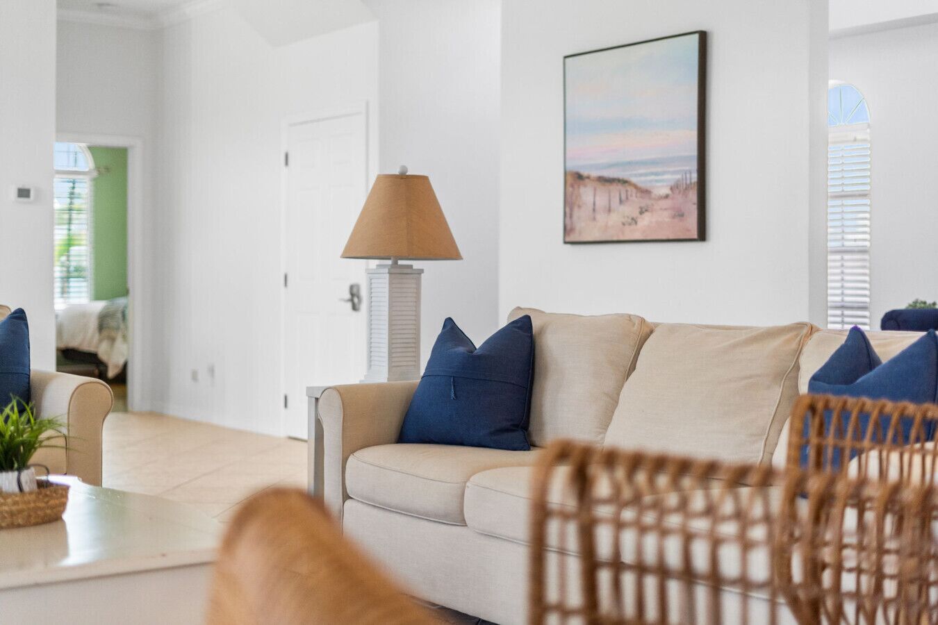 Un salon moderne avec un canapé beige, des coussins bleus, un fauteuil en osier et une lampe.
