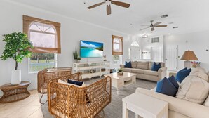Ein geräumiges Wohnzimmer mit Rattanmöbeln, einem Flachbildfernseher und einem Deckenventilator.