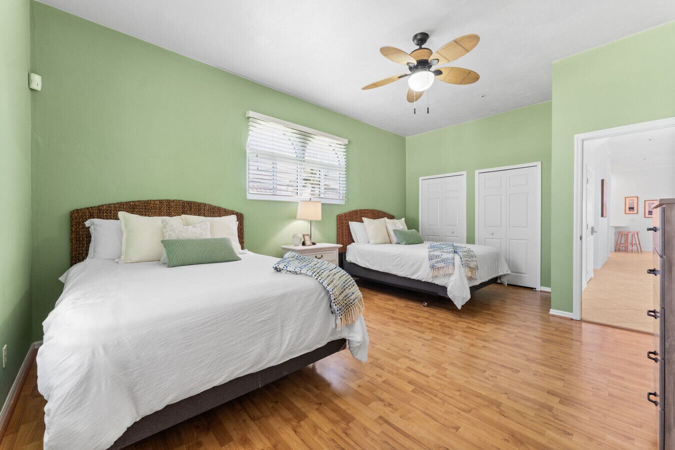 A bedroom with two beds, a ceiling fan, and a window with blinds.