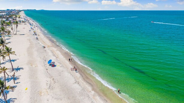 Ein Strand mit klarem türkisblauem Wasser, einem sandigen Ufer und Palmen.