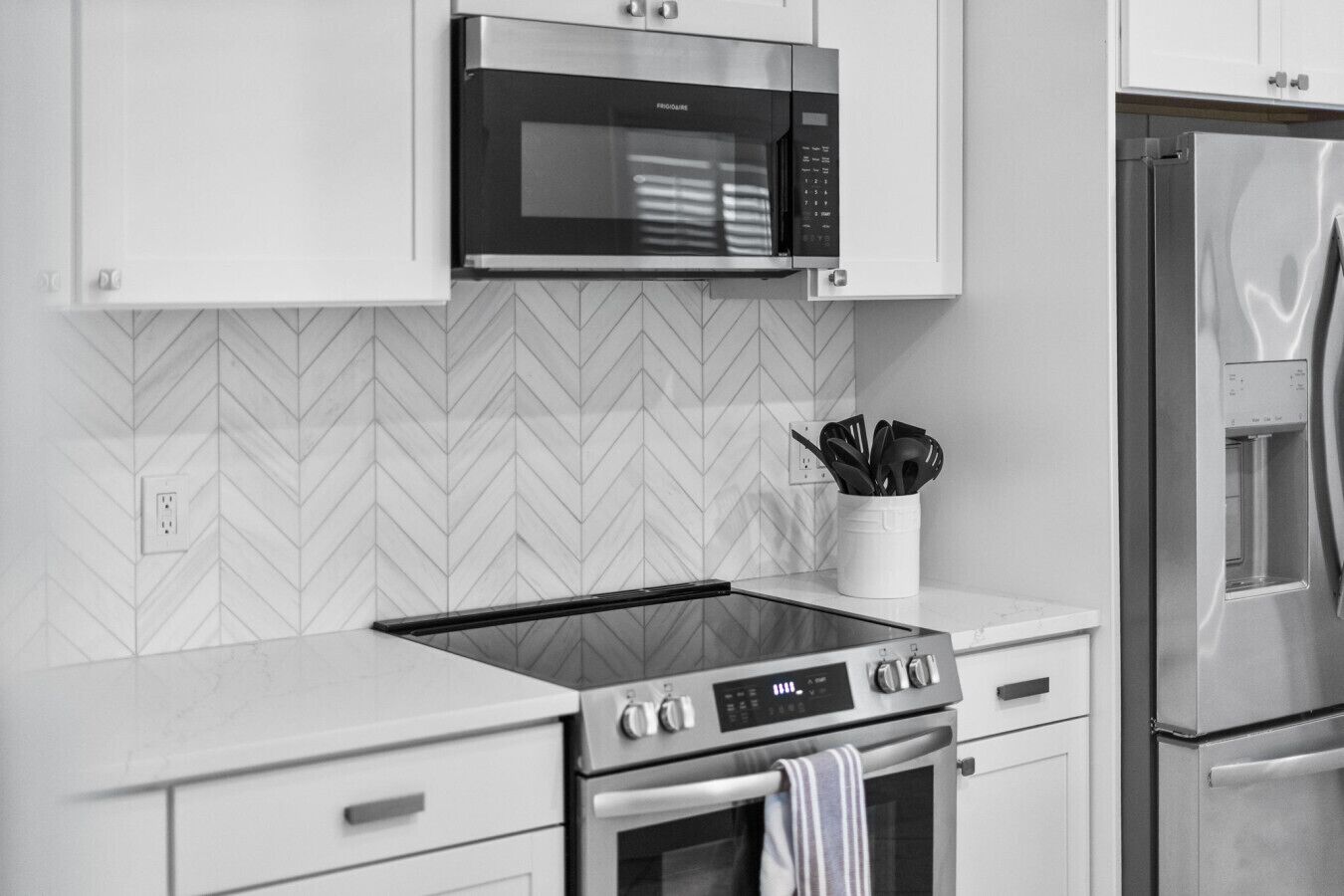 A modern kitchen with a built-in microwave, stainless steel appliances, and a herringbone-patterned backsplash.