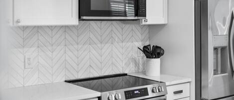 A modern kitchen with a built-in microwave, stainless steel appliances, and a herringbone-patterned backsplash.
