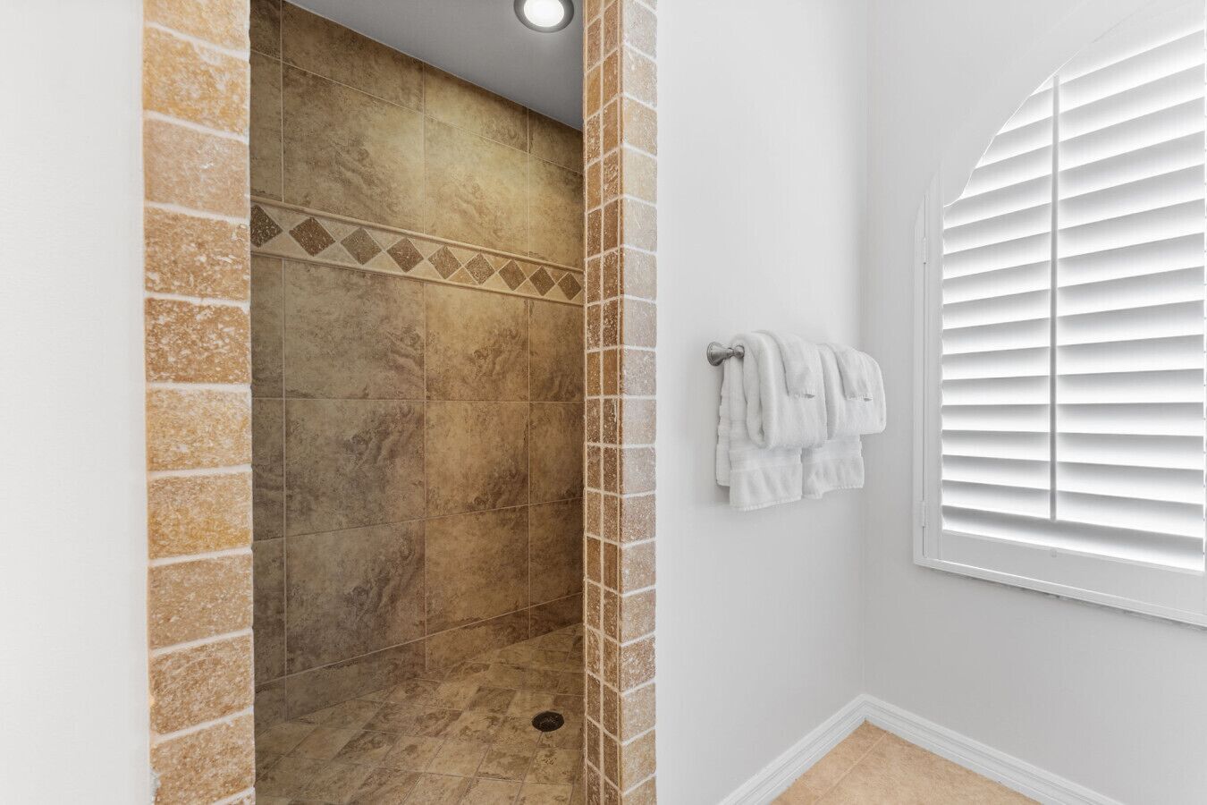 A bathroom with a shower area, tiled walls, and a window with blinds.