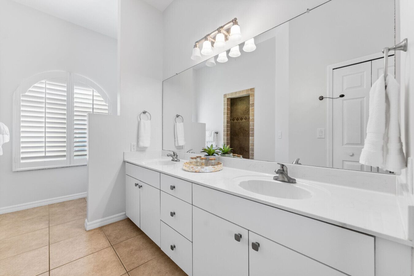 A modern bathroom with a large mirror, white cabinets, and a vanity with a sink.