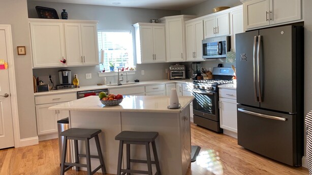 A modern kitchen with white cabinets, a central island, a refrigerator, a microwave, and an oven.