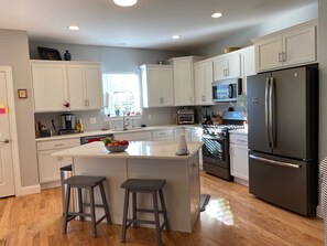Une cuisine moderne avec des meubles blancs, un îlot central, un réfrigérateur, un four à micro-ondes et un four traditionnel.