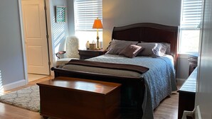 A bedroom with a bed, bedside tables, a wooden chest, a ceiling fan, and a door.