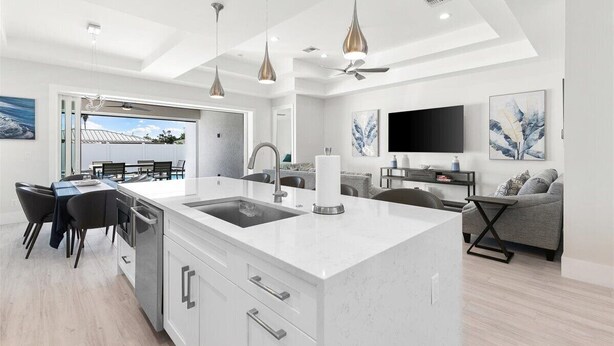 A modern kitchen with a central island, white cabinetry, and pendant lighting. - Brand New Luxury Pool & Spa Home Near Beach! (Naples)