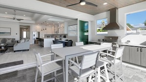A modern kitchen with a central island, white cabinetry, and a large window. - Brand New Luxury Pool & Spa Home Near Beach! (Naples)