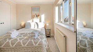 Une chambre d’hôtel avec deux lits, une grande fenêtre, un radiateur et un tableau au mur.
