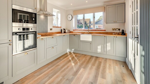 Une cuisine moderne avec des meubles de couleur gris clair, une hotte en acier inoxydable et un plan de travail en bois.