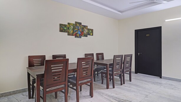 A dining area with a rectangular table and six wooden chairs. There is a black door on the right and a ceiling fan above. - Treebo Lavish Palms (Hyderabad)
