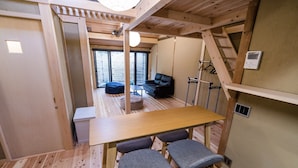 Une petite pièce en bois, avec une table et deux chaises, un canapé et une fenêtre avec des stores.