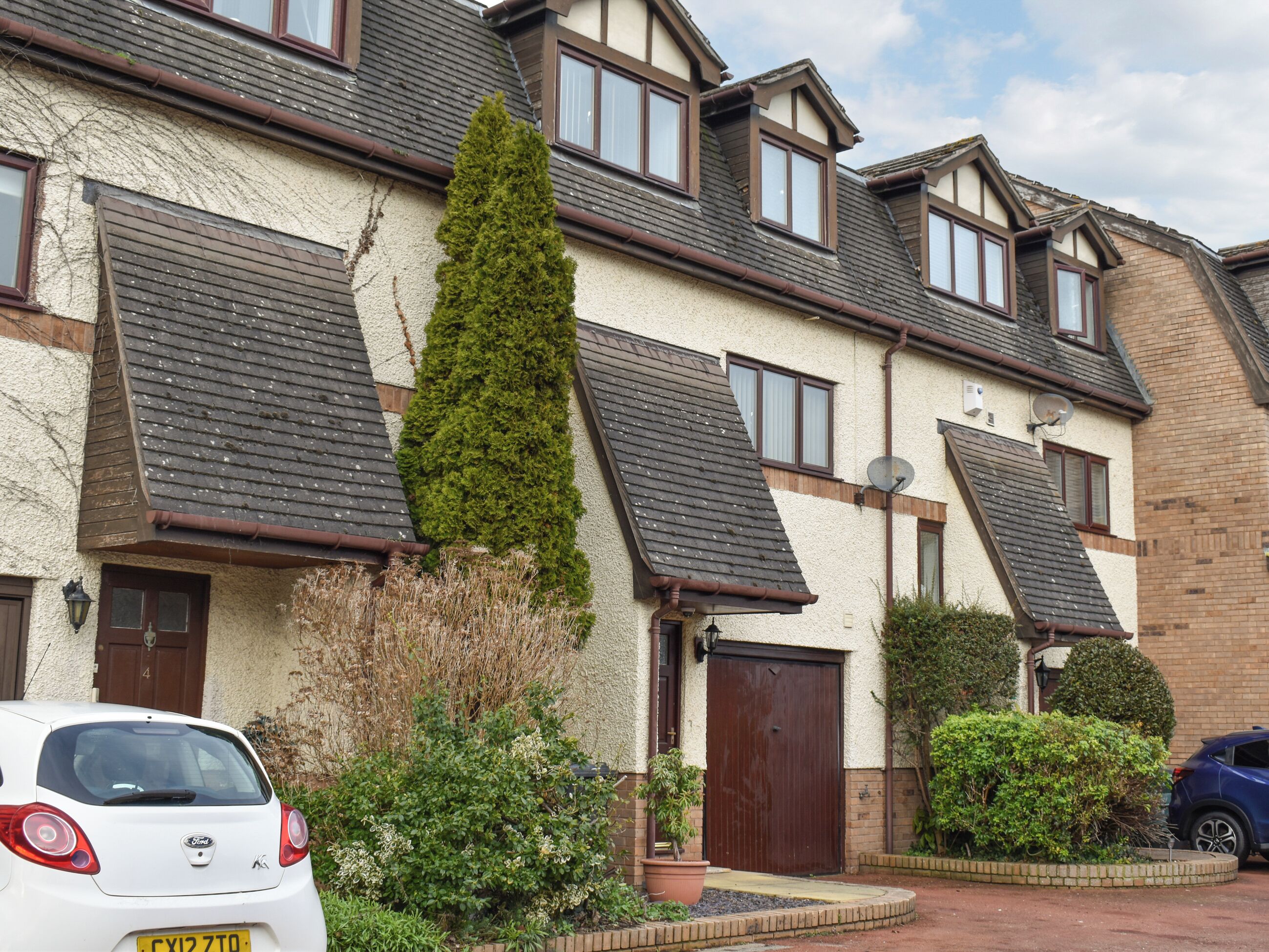 A row of terraced houses with pitched roofs, a central garden, and a car parked in front.