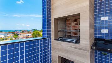 Cozinha com azulejos azuis, forno de tijolos e vista para o mar.