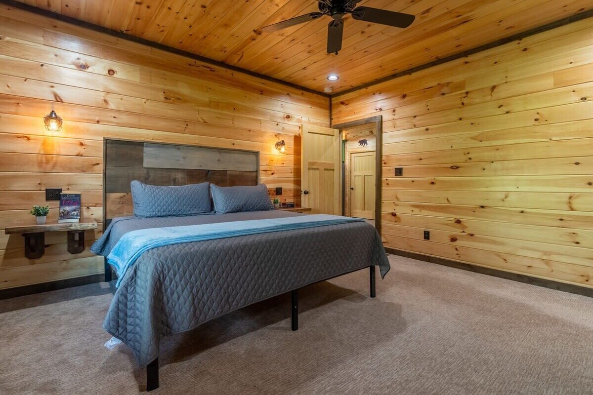Un dormitorio con paneles de madera, una cama, mesitas de noche y un ventilador de techo.
