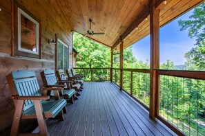 Una terraza de madera con sillas Adirondack, un ventilador de techo y vista a un bosque.