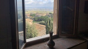 A room with a large window offering a view of a rural landscape, a tiled floor, and a vase on the windowsill. - The Penthouse of Dreams (san gimignano)