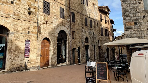A stone building with arched doorways and windows, outdoor seating, and a signboard for a restaurant. - The Penthouse of Dreams (san gimignano)