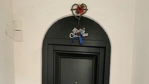 A black door with a decorative sign above it, a small plant beside the door, and a light switch on the wall. - The Penthouse of Dreams (san gimignano)