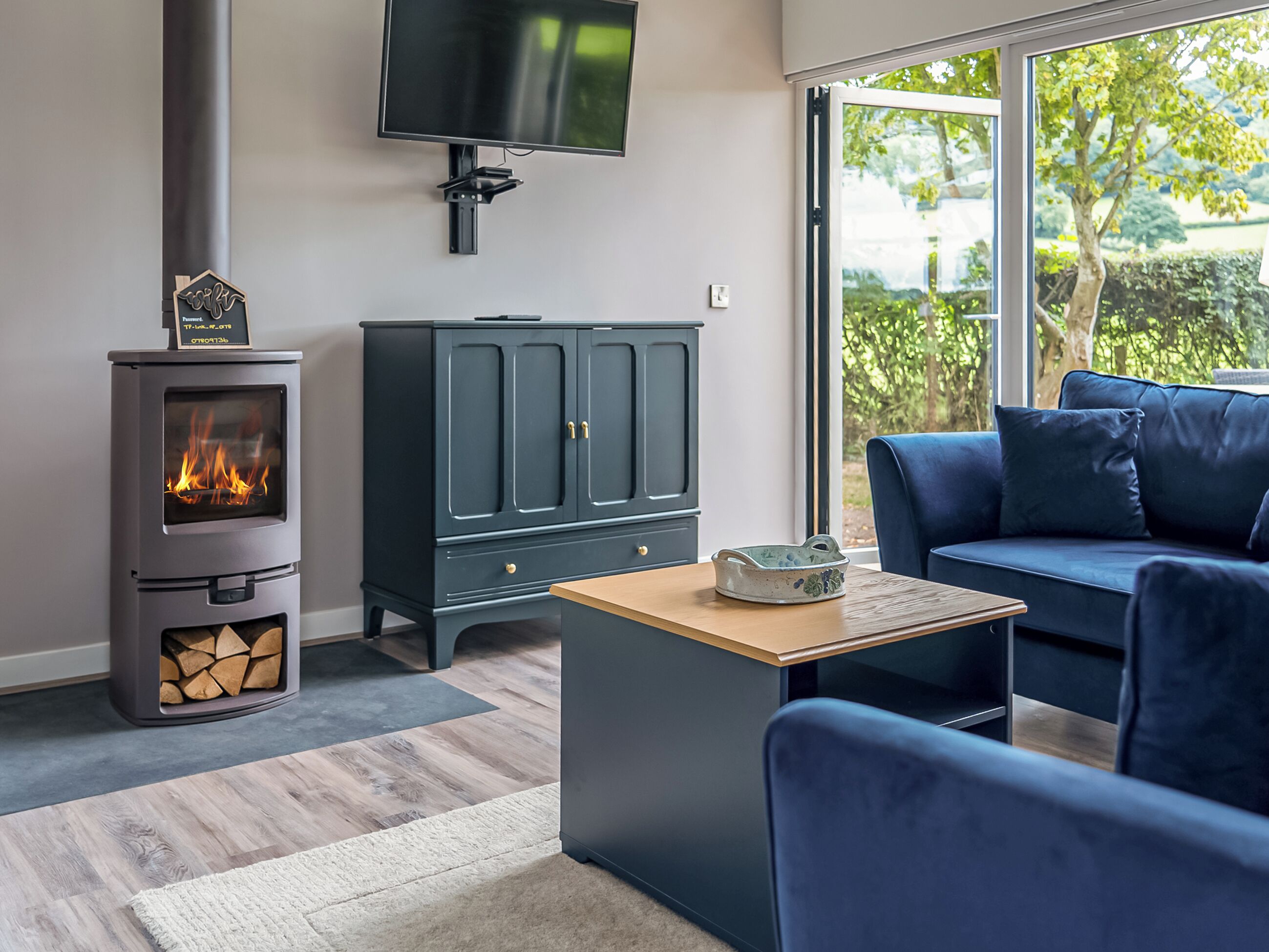 A modern living room with a wood-burning stove, a dark-colored cabinet, a blue sofa, and a television mounted on the wall.