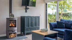 A modern living room with a wood-burning stove, a dark-colored cabinet, a blue sofa, and a television mounted on the wall. - Cuckoo Lodge - UK42541 (Clifford)