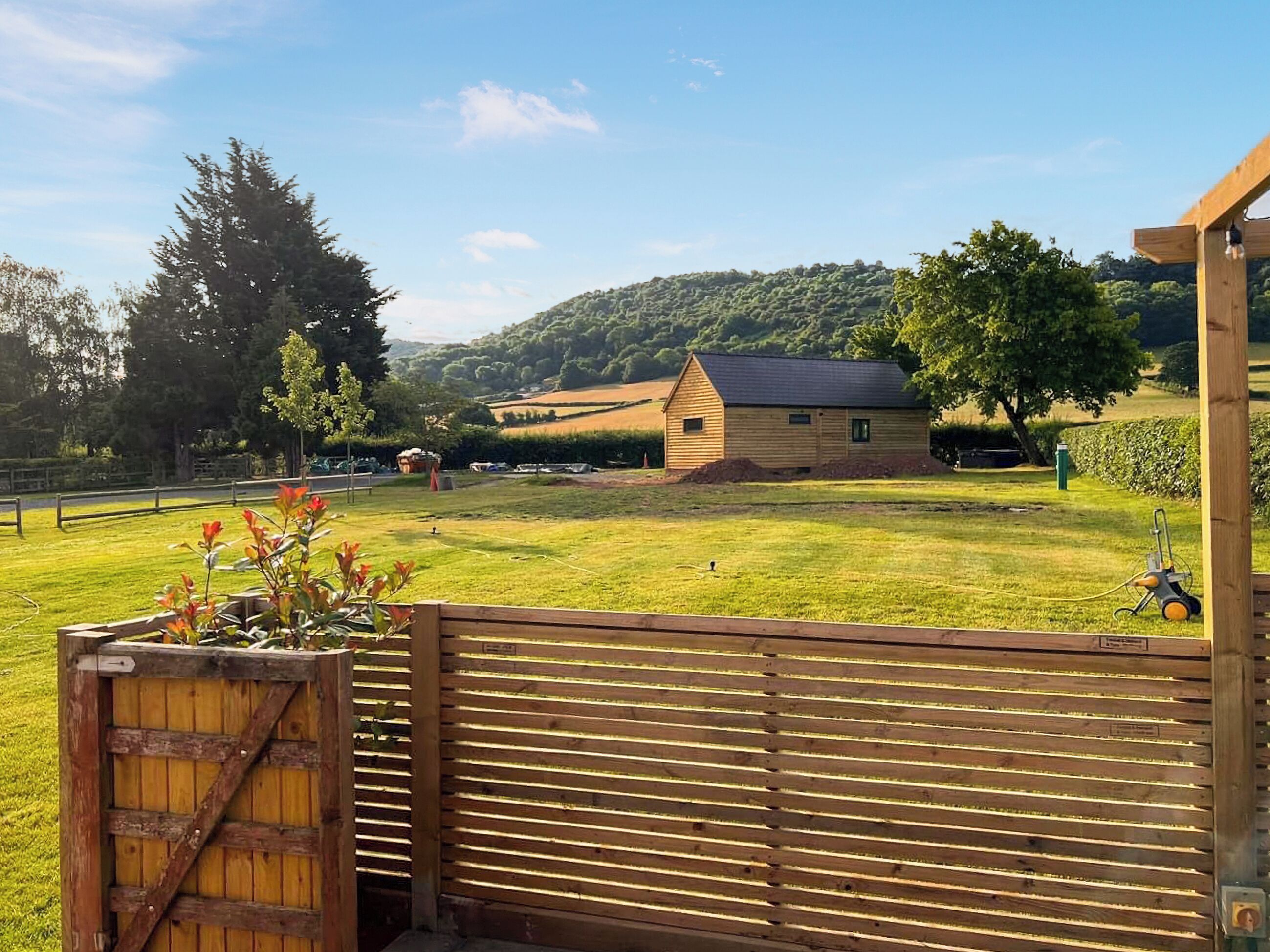 A wooden fence with a gate, a grassy field, a wooden building, and a tree.