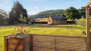 A wooden fence with a gate, a grassy field, a wooden building, and a tree. - Cuckoo Lodge - UK42541 (Clifford)