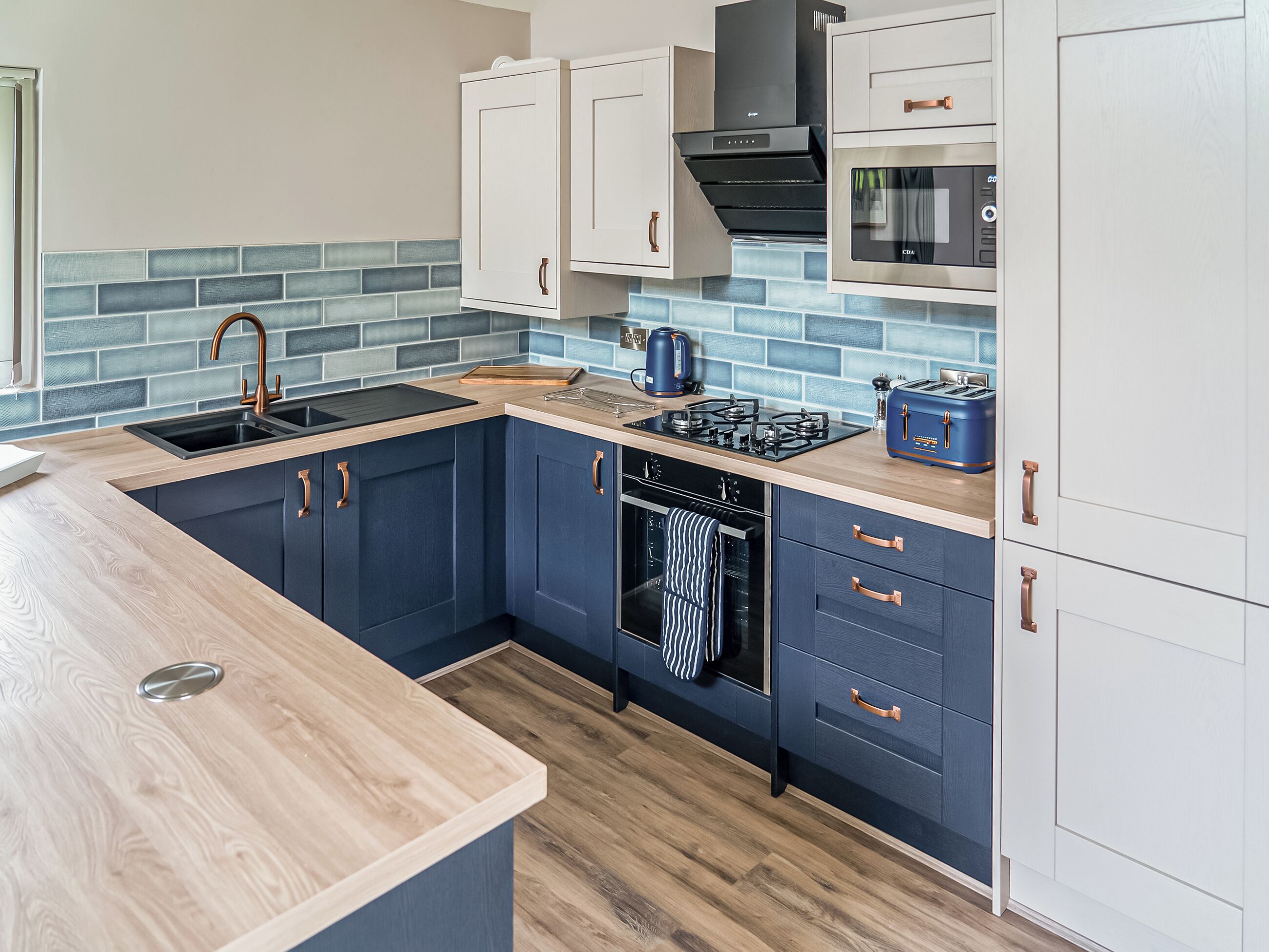 A modern kitchen with dark blue cabinets, a wooden countertop, a gas stove, a built-in oven, and a microwave.