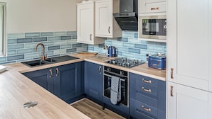 A modern kitchen with dark blue cabinets, a wooden countertop, a gas stove, a built-in oven, and a microwave. - Cuckoo Lodge - UK42541 (Clifford)