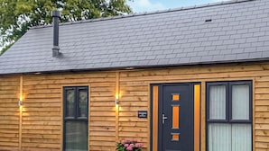 A wooden house with a dark front door, two windows, and a chimney. - Cuckoo Lodge - UK42541 (Clifford)