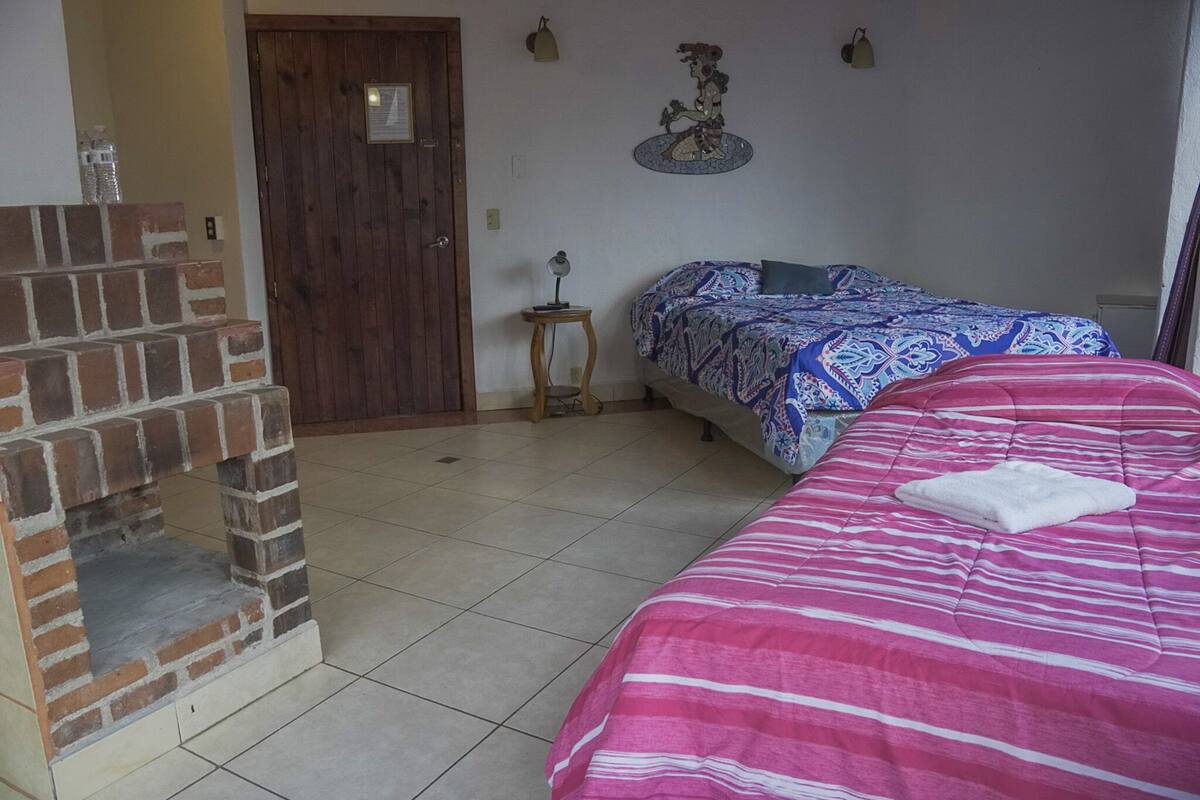 Ein Zimmer mit Kamin aus Ziegelsteinen, einem Bett mit rosa gestreifter Bettdecke und einem gemusterten Überwurf.