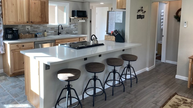 Una cocina moderna con gabinetes de madera, una isla grande con taburetes de bar, un microondas empotrado y un refrigerador.
