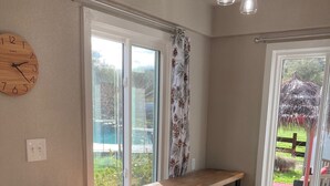 Una cocina con mostrador de madera, cuatro taburetes, un reloj y una ventana con cortinas.