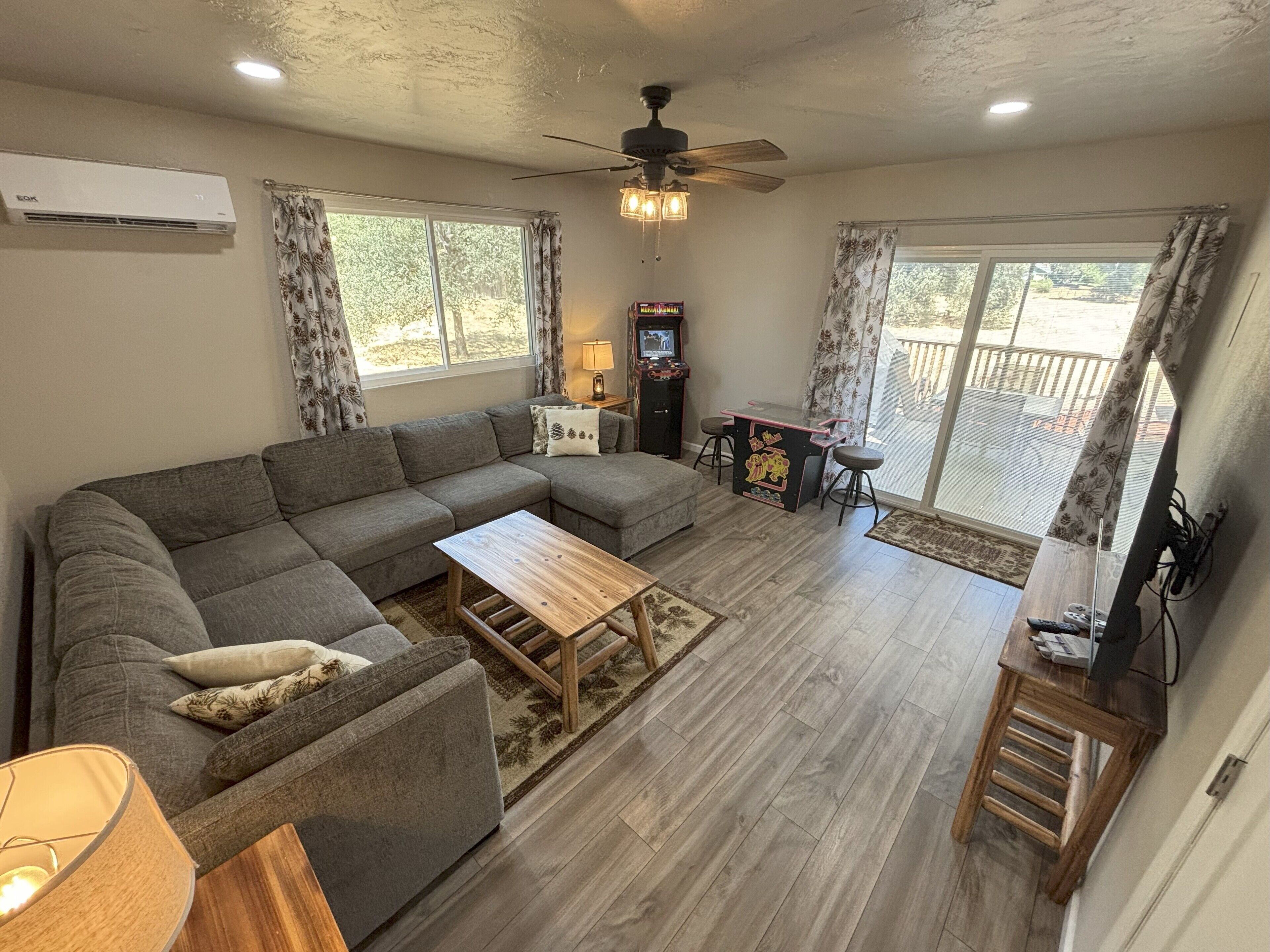 A living room with a sectional sofa, a wooden coffee table, a ceiling fan, and a small table with a lamp.