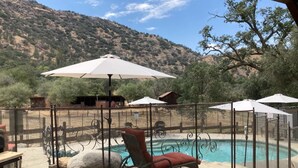 Zona de piscina con una silla reclinable roja, una sombrilla blanca y vistas a un paisaje montañoso.
