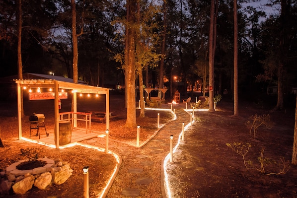 A rustic outdoor seating area with a fire pit, wooden tables, and string lights.