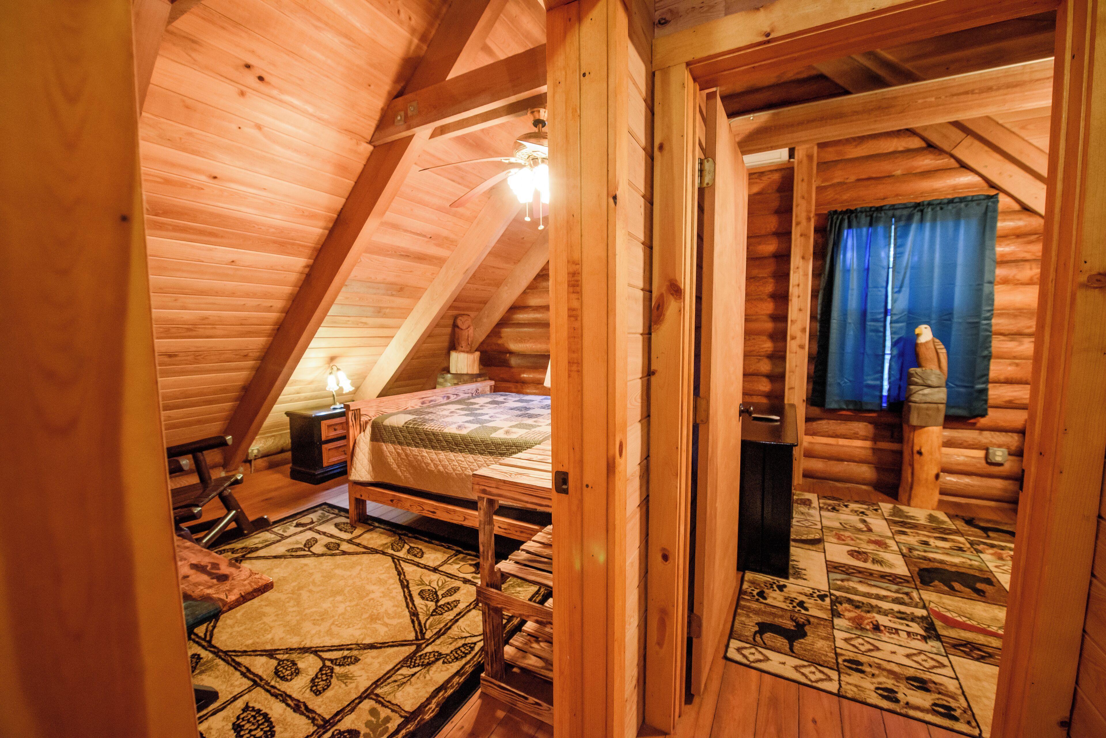 Un dormitorio tipo cabaña de madera con cama en altillo, techo de madera y ventana con cortinas.