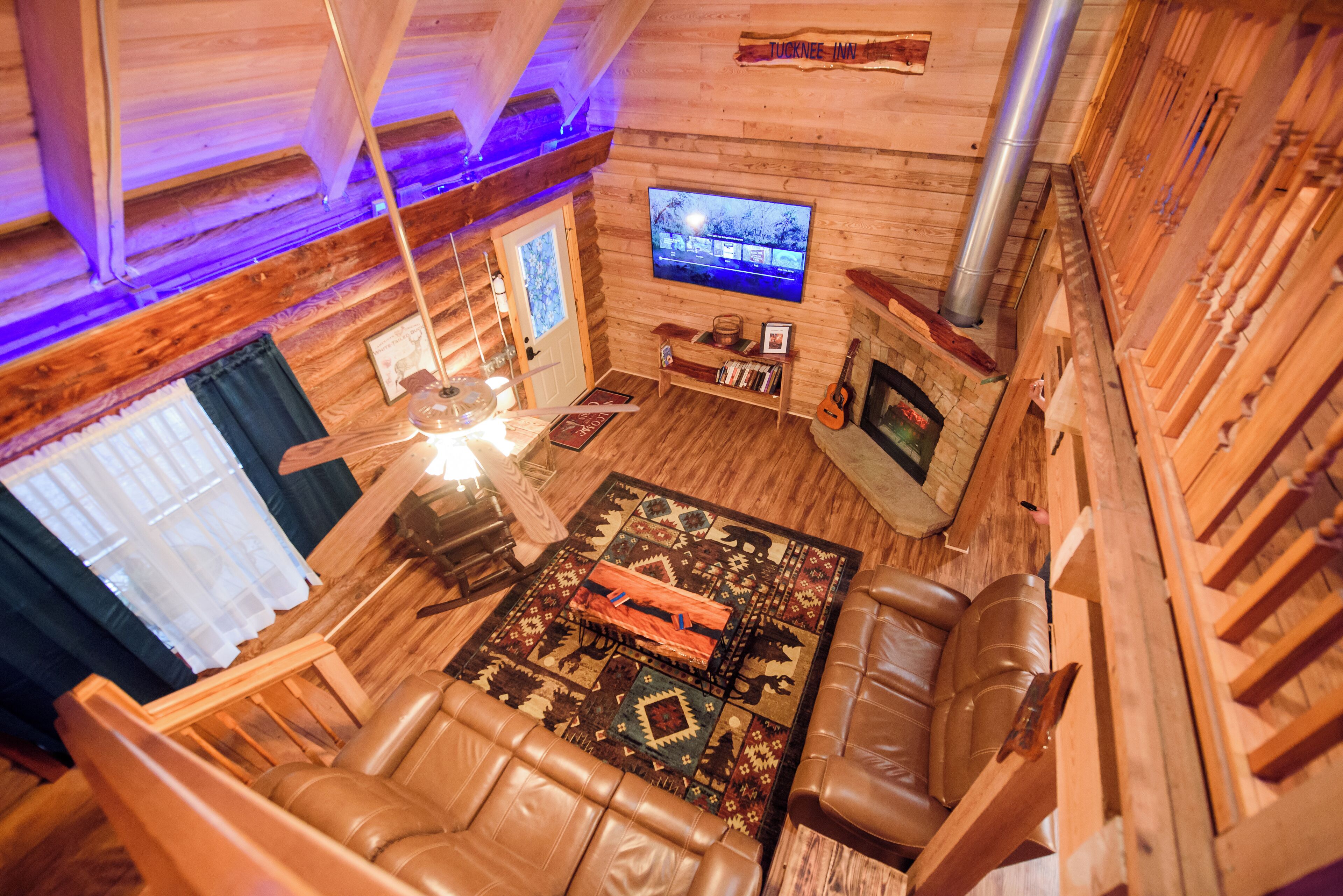 Un acogedor interior de cabaña de madera con chimenea, sofá de cuero y televisor montado en la pared.