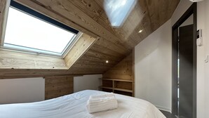 Een slaapkamer met dakraam, houten plafond, een bed met witte beddengoed en een inloopkast.