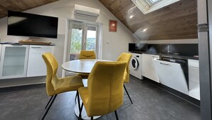 Een moderne keuken met dakraam, een eethoek met gele stoelen, en een flatscreen televisie boven de aanrecht.