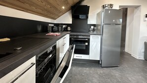 Een moderne keuken met een zwart aanrecht, roestvrijstalen apparatuur en een houten plafond.