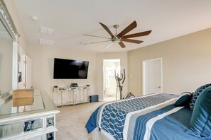 Camera da letto con un letto, ventilatore a soffitto, televisione, comò e una porta che dà su un'altra stanza.